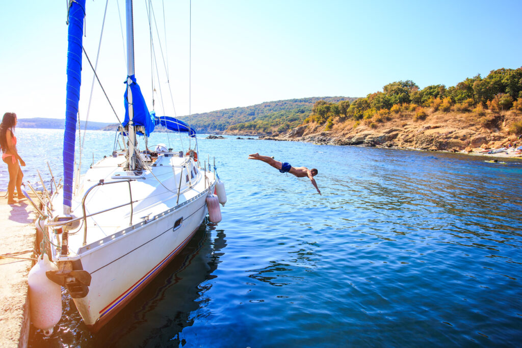 Young people having fun on yacht, diving into water. Kids or child