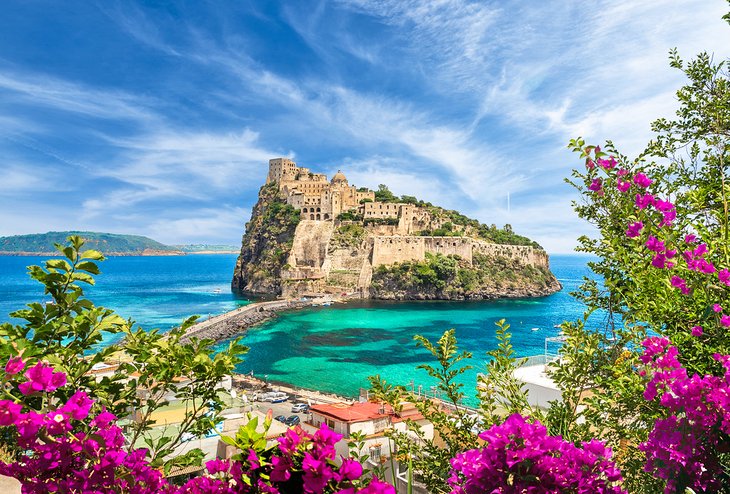 A panoramic view of the rugged coastline of Ischia, with rocky cliffs, crystal clear water, and lush green vegetation.